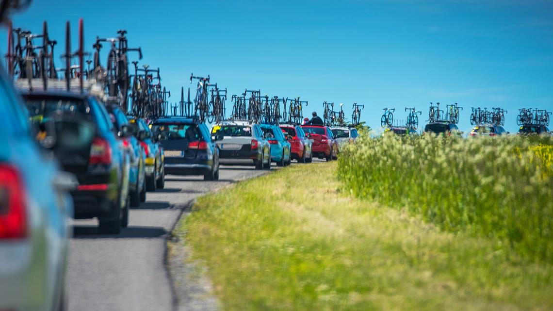 Długa kolejka samochodów z licznymi rowerami dla uczestników Tour de France.